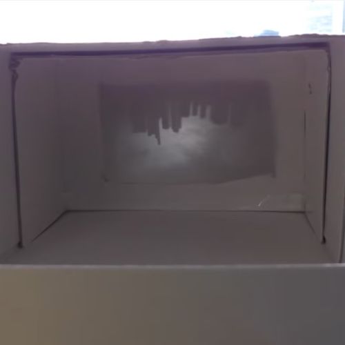 Durch eine Schachtel aus Pappe mit Loch kann man das umgedrehte Bild einer Stadt mit Hochhäusern sehen.