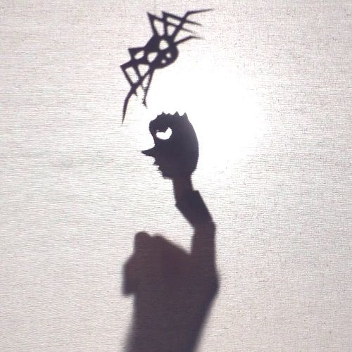 Der Schatten von einer gebastelten Spinne und einer Fingerpuppe von einem Prinzen mit Krone.
