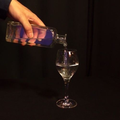 Eine Hand schüttet Wasser in ein halbvolles Glas.