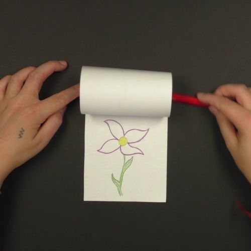Zwei Hände rollen ein Blatt mit einem Stift auf, auf dem Blatt darunter ist eine bunte Blume gemalt.