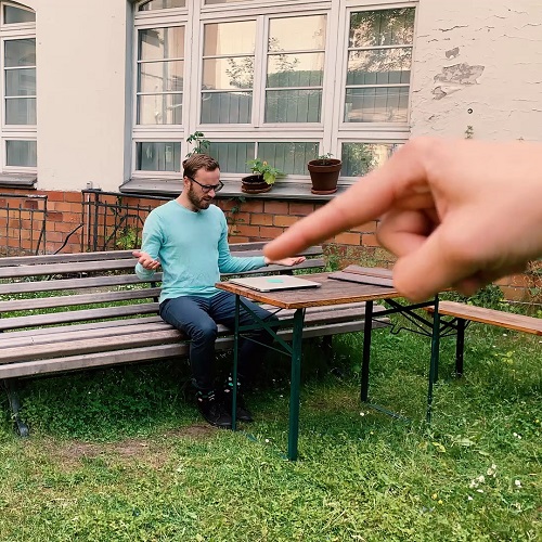 Ein Mann sitzt auf draußen auf einer Bank und eine riesige Hand hat seinen Laptop zugeklappt.