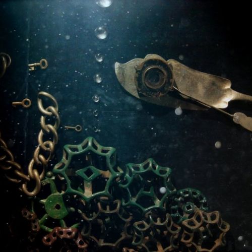 Ein Fisch aus einem Dosenöffner schwimmt über Korallen aus Metallketten vor einem blauen Hintergrund.